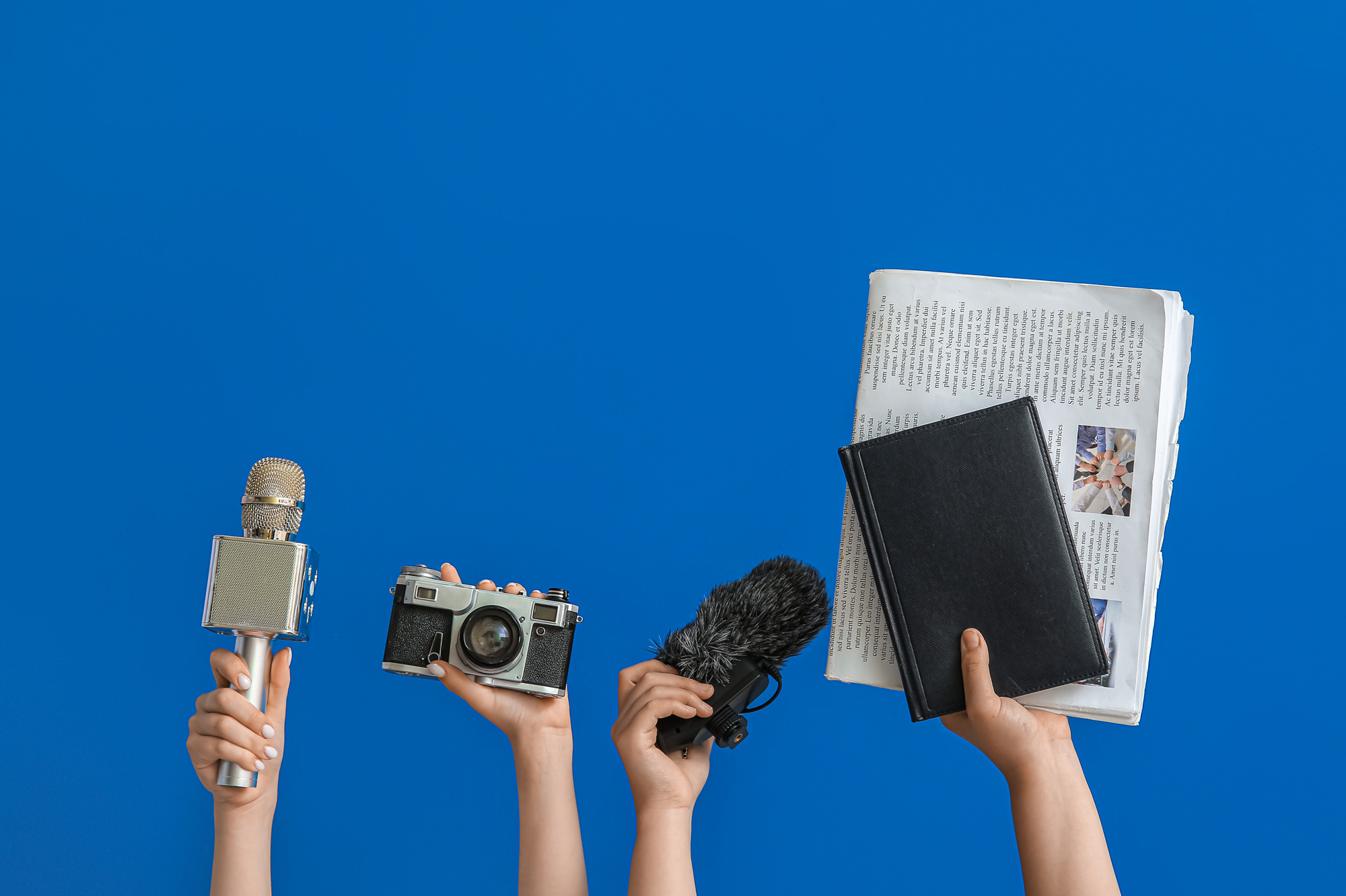 Hände halten verschiedene Objekte für die Pressearbeit in die Höhe (Mikrofon, Kamera, Notizbuch, Zeitung)