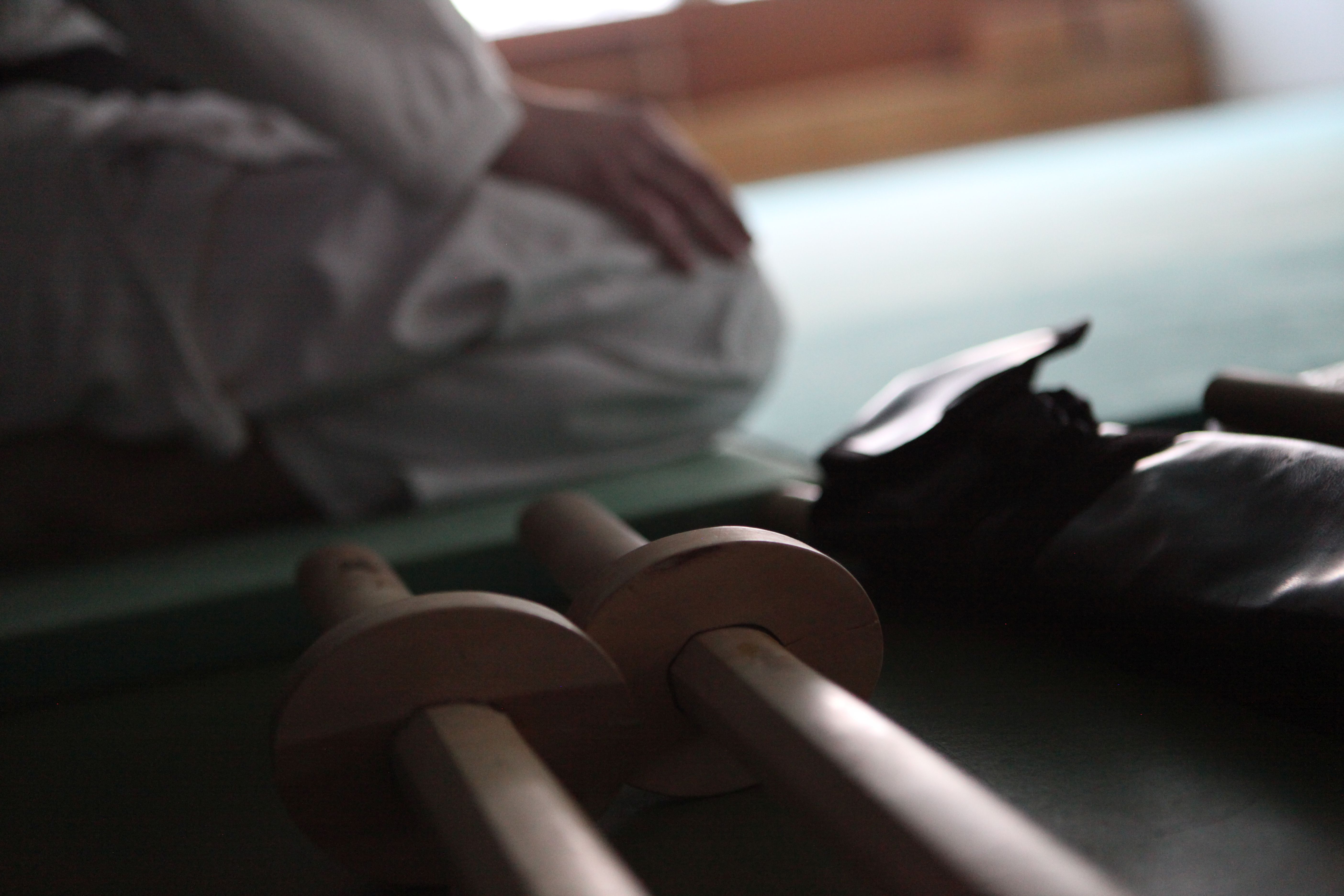 Aikido-Schwerter liegen bereit am Rand der Trainingsfläche. Ein Aikidoka sitzt auf der Matte.